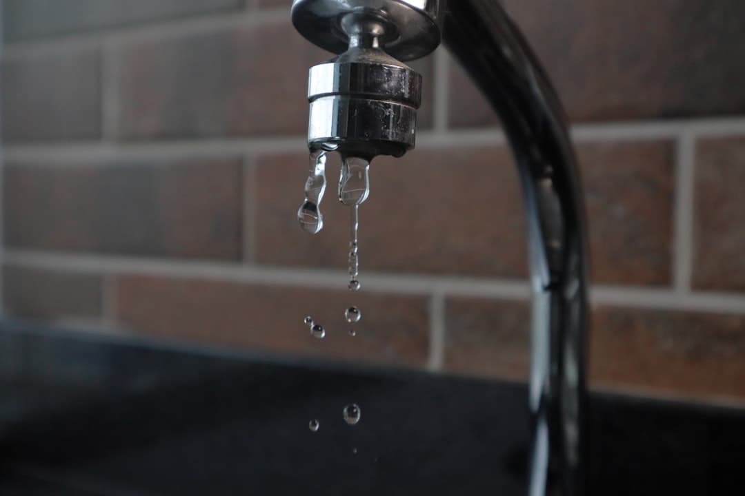 Robinet en métal avec des gouttes d'eau qui tombent, sur fond de mur en briques.