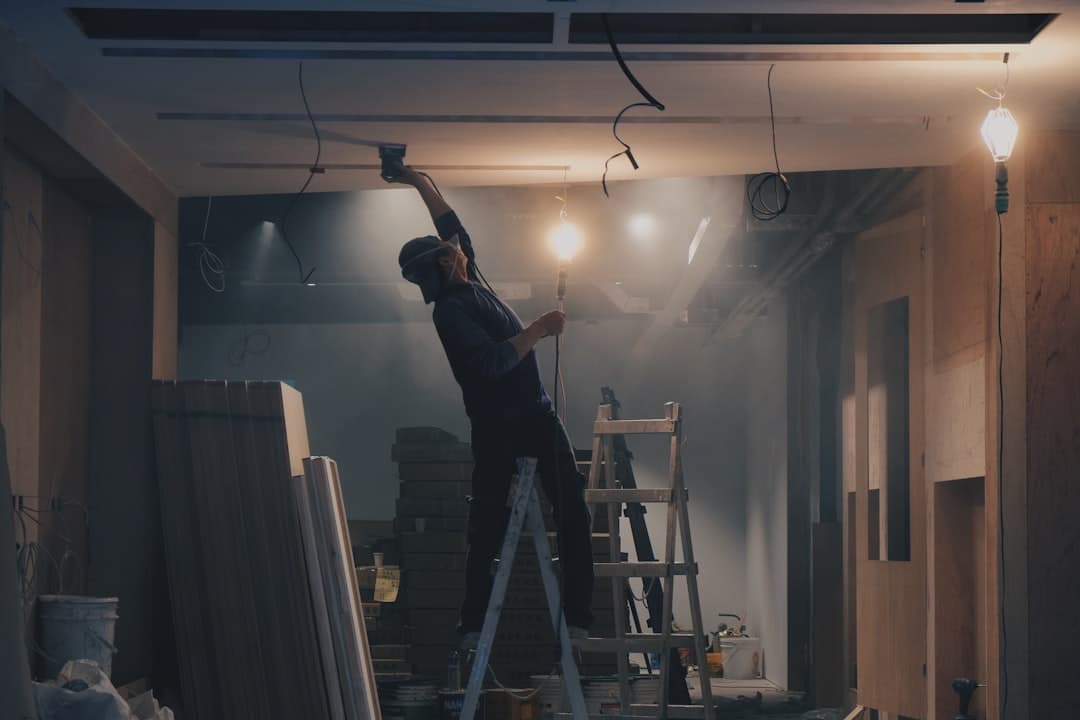 Un technicien effectuant des travaux d'électricité dans un espace de chantier, avec un éclairage tamisé et des matériaux autour.